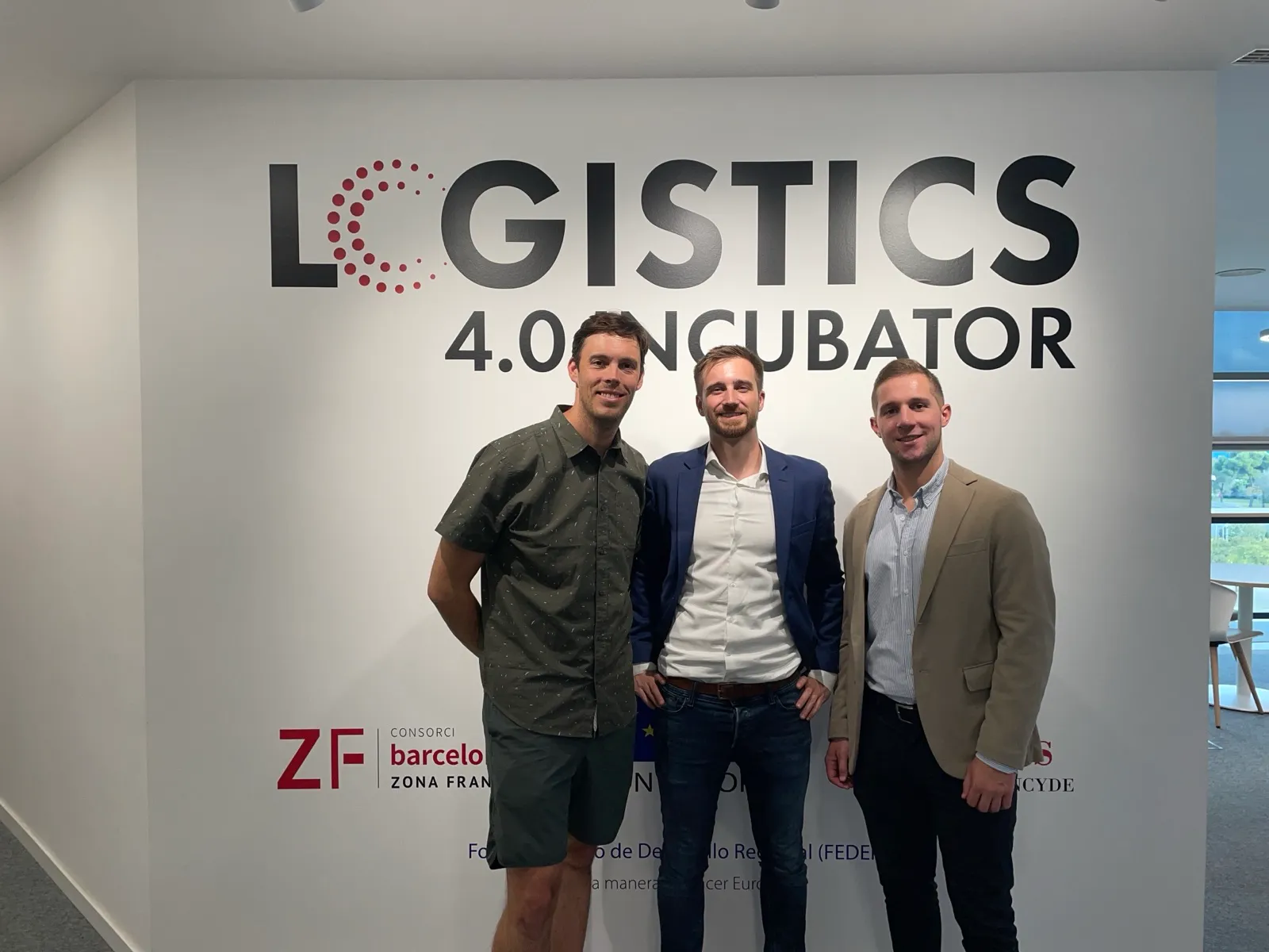 The three Grasshopper co-founders in front of the Logistics 4.0 Incubator wall in Barcelona, June 2024.